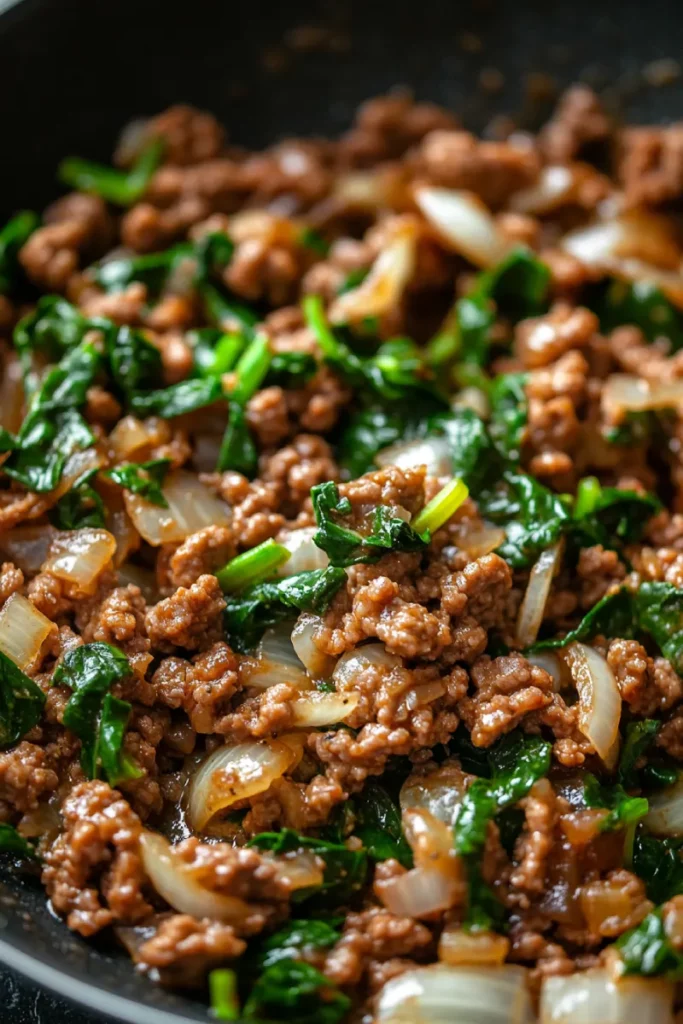 Ground beef and spinach cooking in skillet with garlic and onion